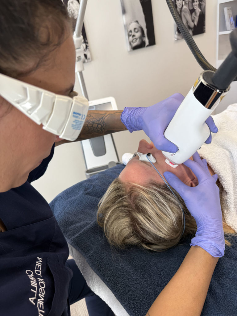liegende Dame mit schutzbrille wird von einer Dame mit einem Lasergerät im Gesicht behandelt